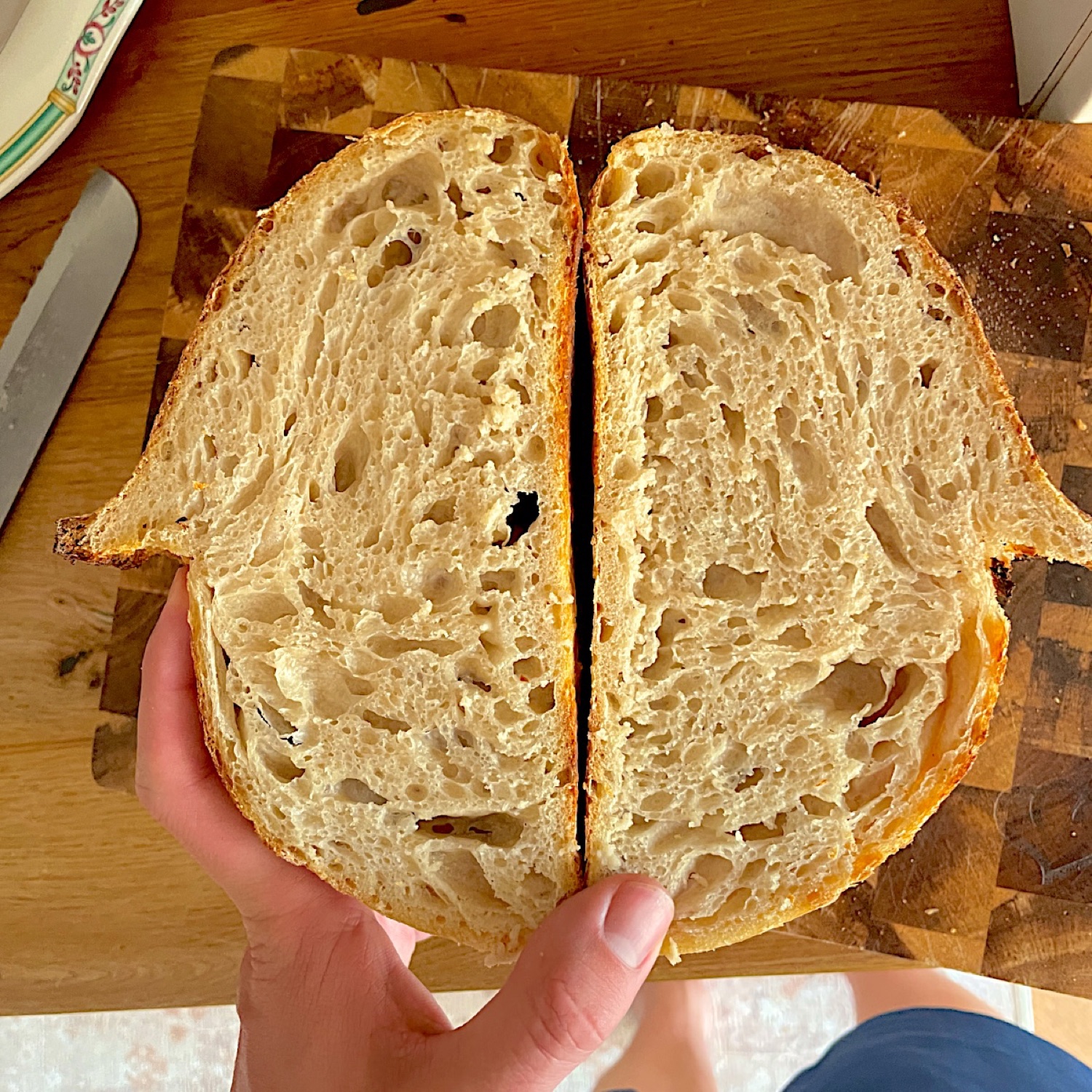 A sourdough loaf cut in half, held up to show the open crumb